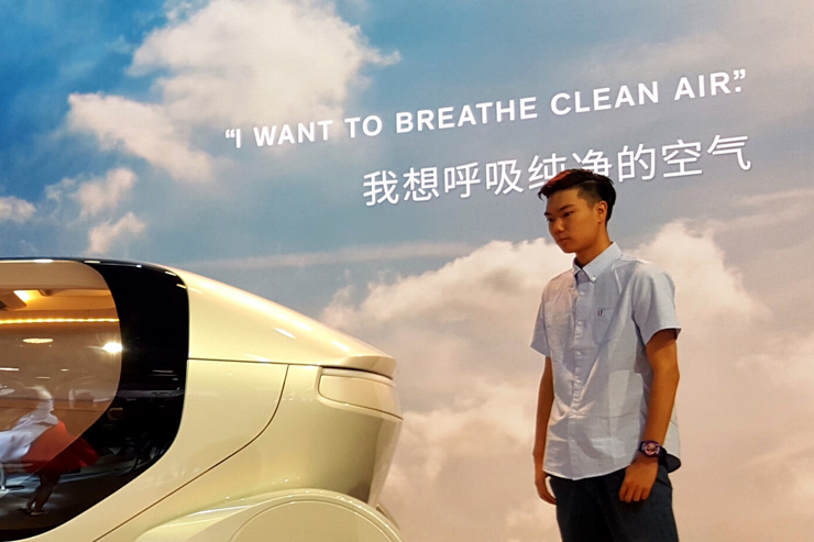 Ein junger Chinese betrachtet auf einer Messe den Prototyp eines futuristischen Autos; im HIntergrund prangt auf einem Pakat der Schriftzug «I want to breathe clean air.»