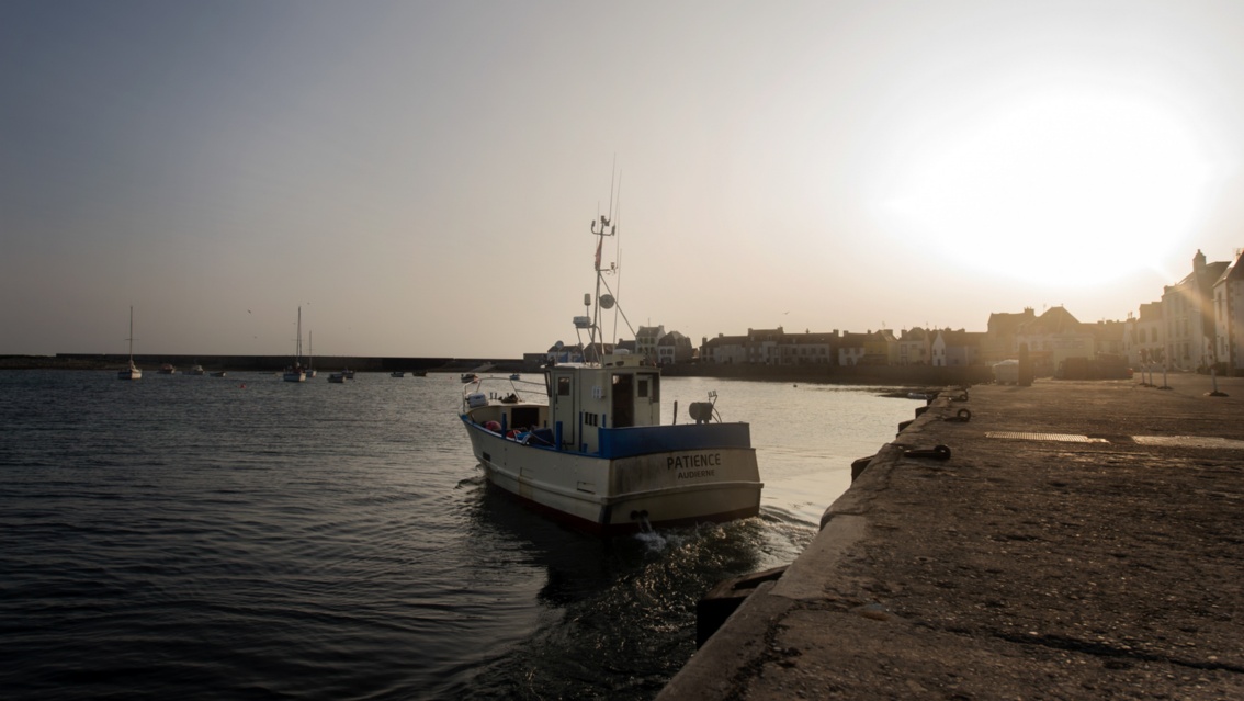 Das kleine Fischerboot setzt in der Abendsonne von der Hafenmole ab.