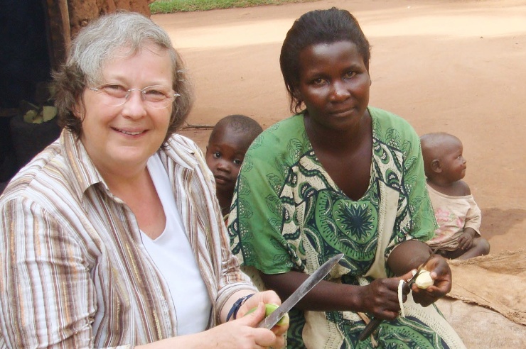 Bärbel Höhn sitzt gemeinsam mit einer ugandischen Mutter und zwei kleinen Kindern vor einem Haus und bereitet eine Mahlzeit vor.