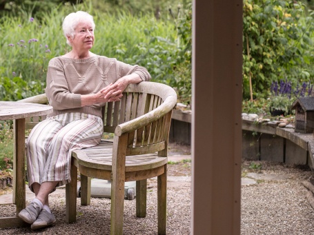 Eine ältere Dame mit kurzen grauen Haaren sitzt auf ihrer Terrasse.