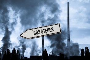 Rauchende Schlote in bläulicher Dämmerung mit Straßenschild, auf dem «CO2-Steuer» steht.