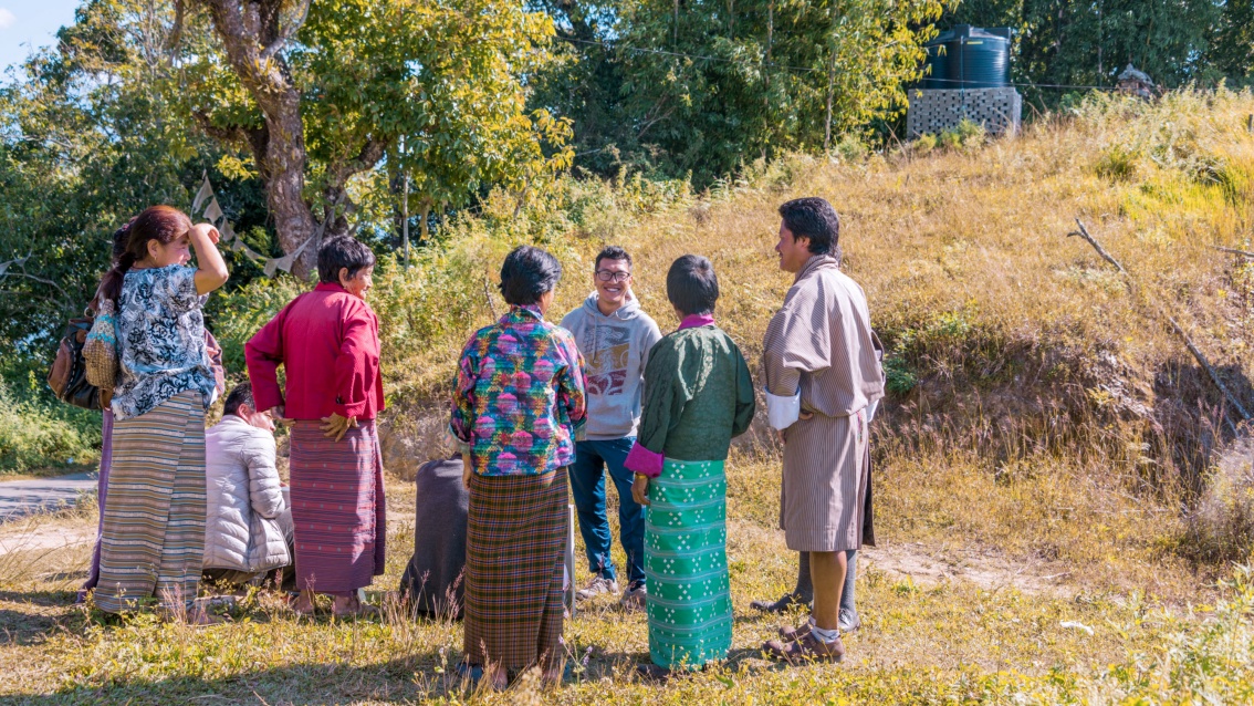 Am Rande eines Weges stehen und sitzen acht Bhutanesen und plaudern entspannt.