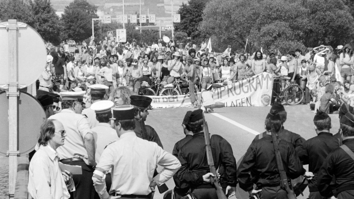 Historisches schwarz-weiß Foto: ein Demozug mit zahlreichen Menschen steht französischen Polizisten, deren Rücken man sieht, gegenüber. 