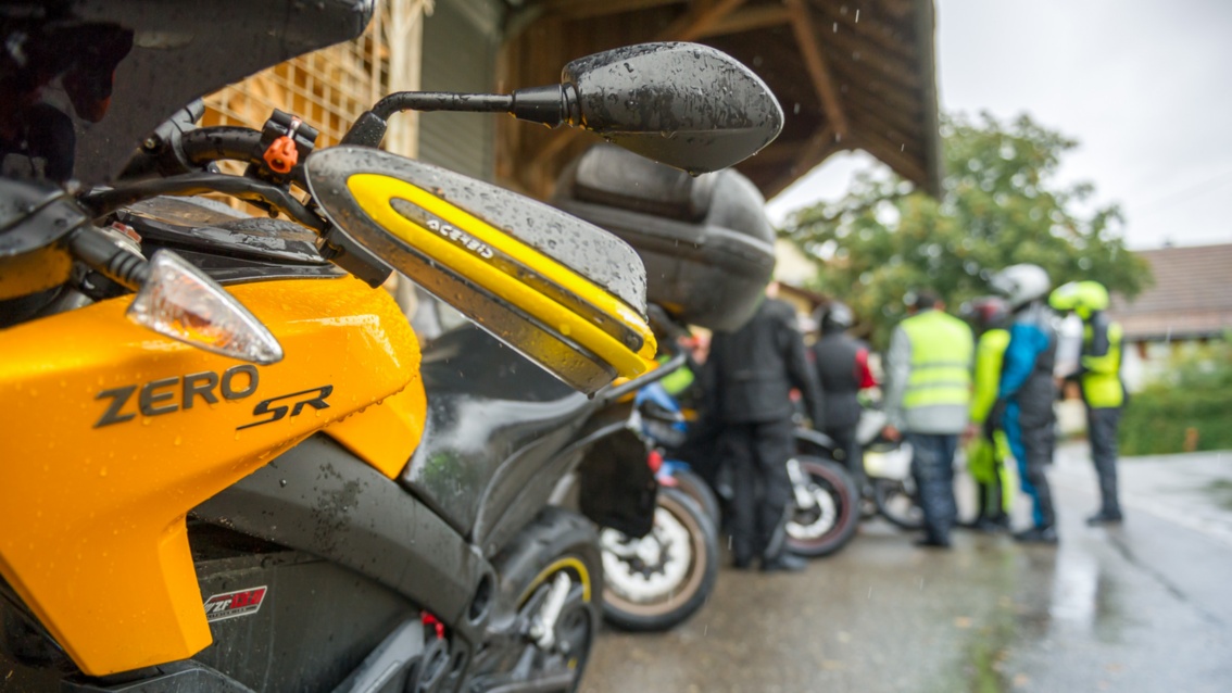 Nahaufnahme eines gelben Motorrades, im Hintergrund ein paar Biker in Regenkluft.