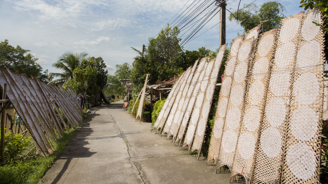 An einem Weg stehen etwa drei Meter hohe Bambusgestelle, auf denen jeweils viele hauchdünne pizzagroße Teigfladen trocknen.