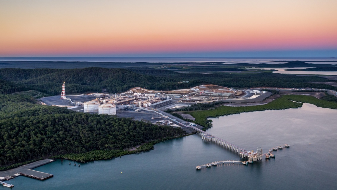 Luftaufnahme einer weitläufigen Küstenlandschaft mit einer Industrie- und Hafenanlage m Sonnenuntergang.