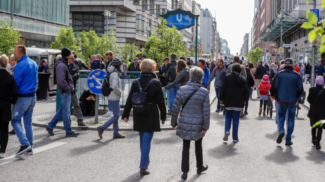 Zahlreiche Fußgänger bevölkern die Berliner Friedrichstraße. Im Hintergrund ist der U-Bahn-Eingang zu sehen.