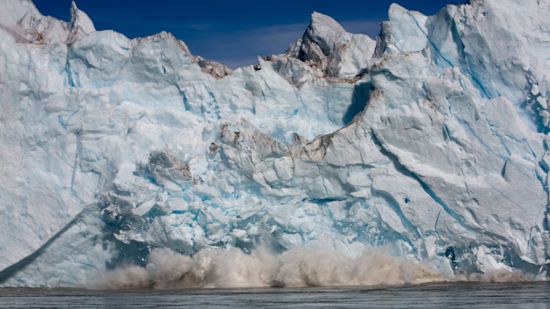 Von einer Gletscherfront bersten riesige Teile und fallen ins Wasser.