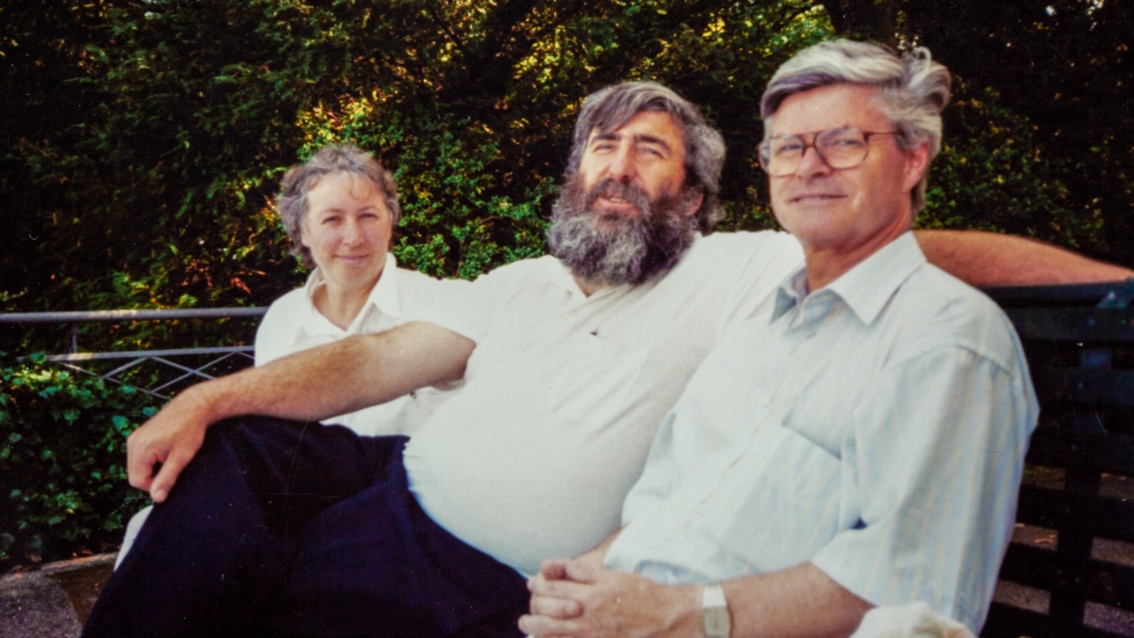 Auf einem historischen Foto sitzen eine Frau und zwei Männer auf einer Parkbank, alle sind etwa in den Vierzigern.