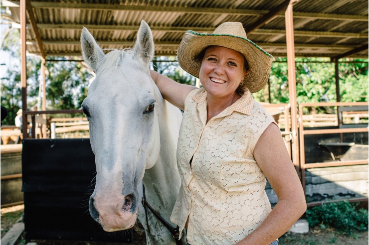 Portrait von Sally Hunter, lachend hat sie den Arm um den Kopf ihres Pferdes gelegt.