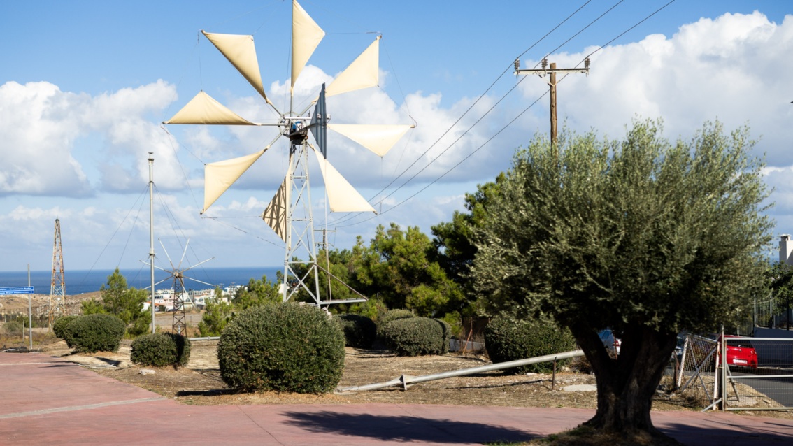A somewhat antiquated-looking wind turbine with eight triangular wind sails stands next to a power line. 