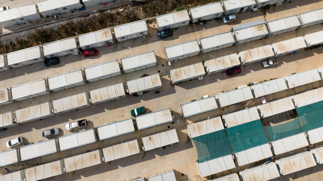 A bird's eye view: numerous residential containers stand in several rows - with cars parked in between. 