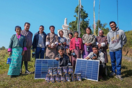 Gruppenfoto von Menschen in asiatisch anmutenden Gewändern, hinter ihnen Gebetsflaggen, vor ihnen zwei Photovoltaik-Module