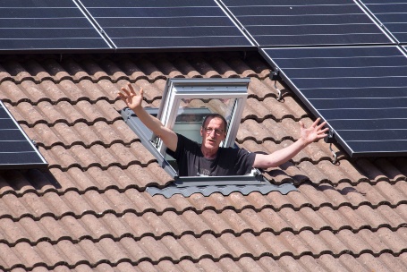 Ein Mann winkt aus einem Dachfenster, um ihn herum sind PV-Module installiert
