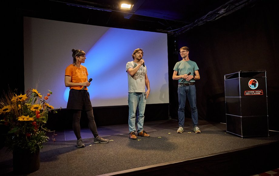 Drei Menschen stehen auf einer Bühne.
