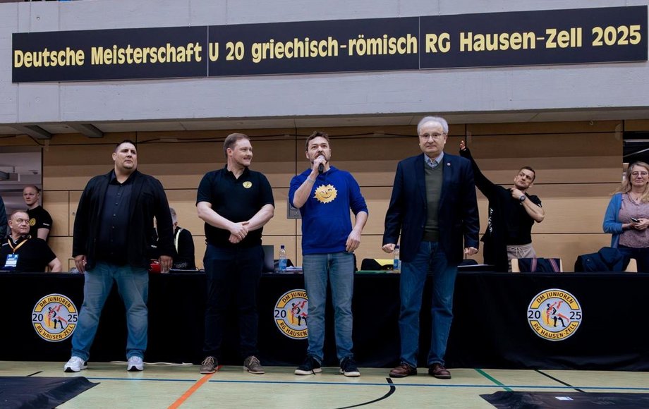 Vier Männer stehen nebeneinander, einer spricht in ein Mikrofon