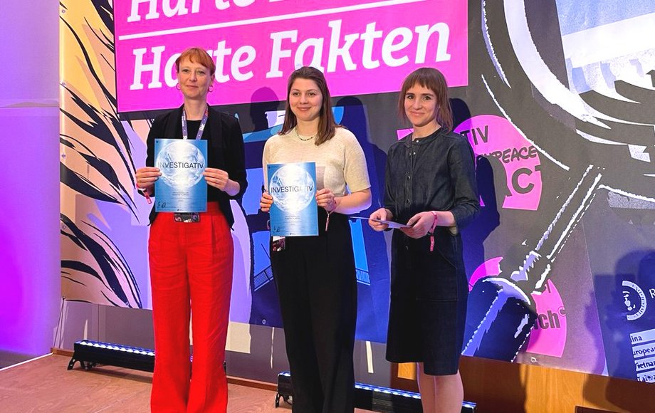 Dei Frauen stehen auf einer farbenfrohen Bühne mit Urkunden in der Hand