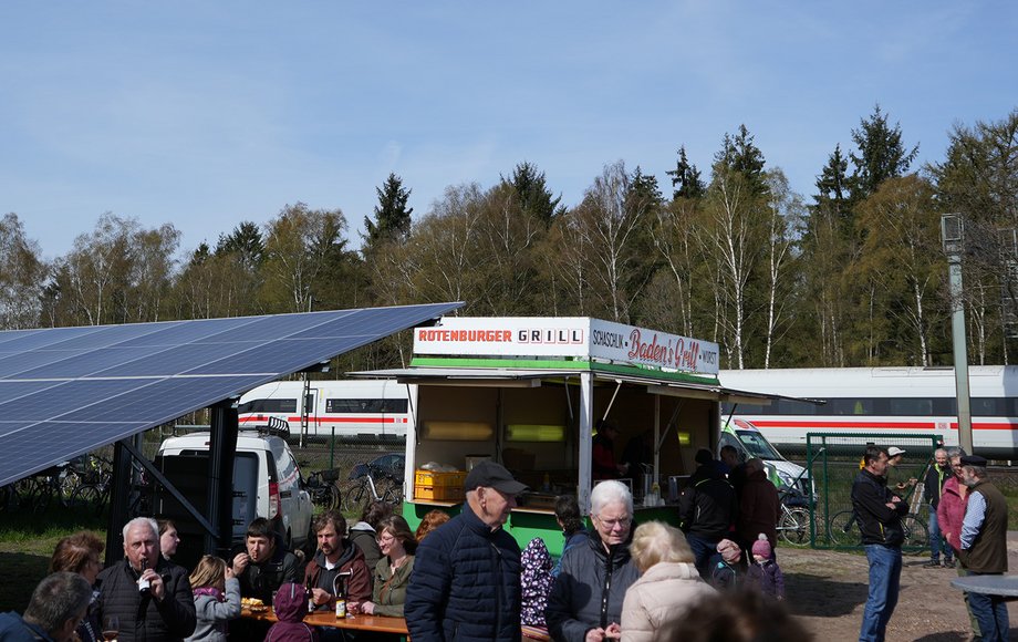 Viele Menschen zwischen PV-Modulen, Imbisstand und Biergarnituren