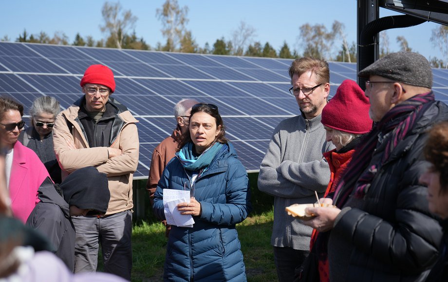 Frau steht umringt von mehreren Menschen vor der Kulisse von Solarmodulen