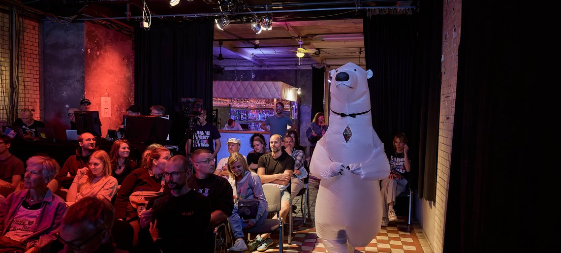 Voll besetzter Zuschauerraum, durch den ein Mensch im Eisbärkostüm läuft.