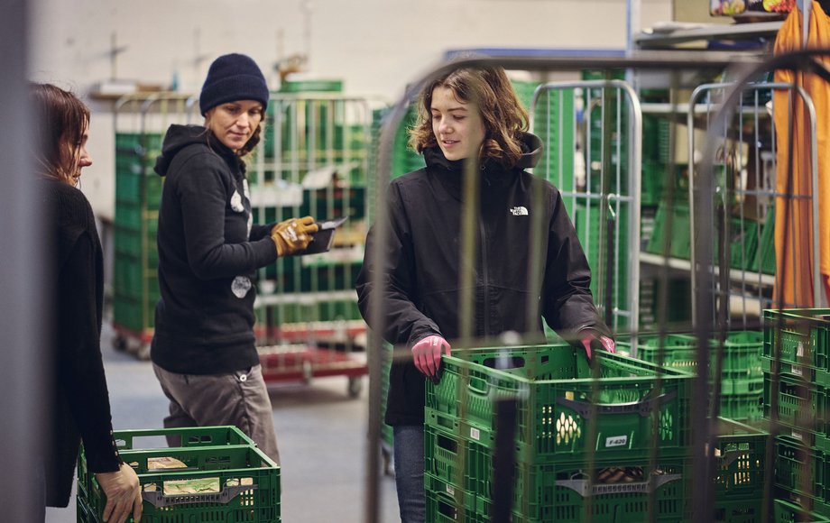 Zwei junge Frauen befüllen eine Kunststoffkiste mit Gemüse