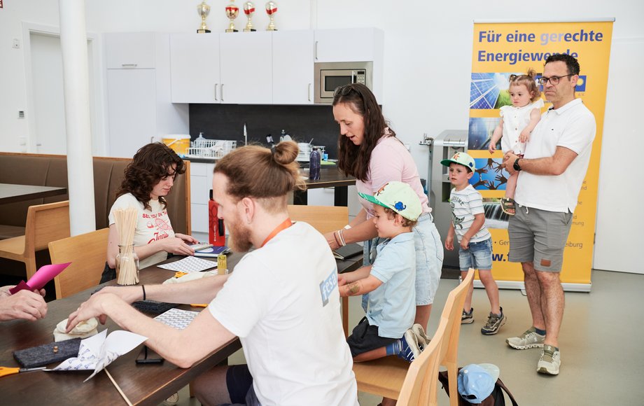 An einem Tisch sitzen ein junger Mann, eine junge Frau und ein Vater mit kleinem Sohn und basteln zusammen