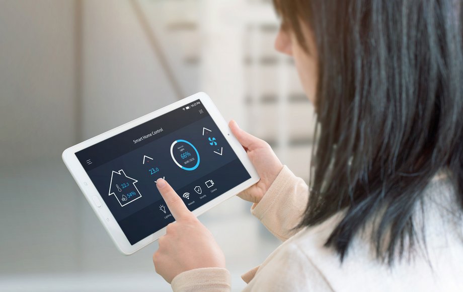 Frau guckt auf ein Tablet, auf dem eine Smart-Home-Oberfläche zu sehen ist.