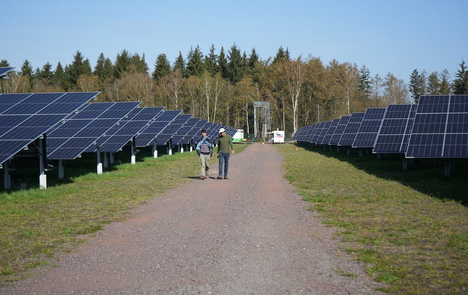 Zwei Menschen spazieren auf einem Weg, der von Solarpaneelen gesäumt wird