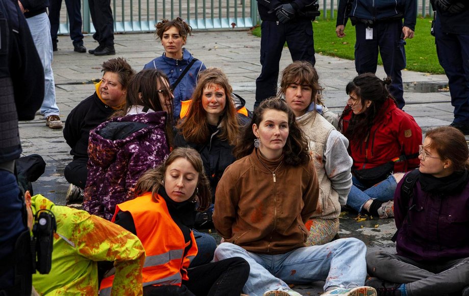 Gruppe von Aktivist:innen der Letzten Generation sitzt auf der Straße umringt von der Polizei