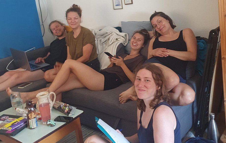Eine Gruppe von vier lachenden jungen Frauen und einem jungen Mann sitzt auf und vor einer Couch.