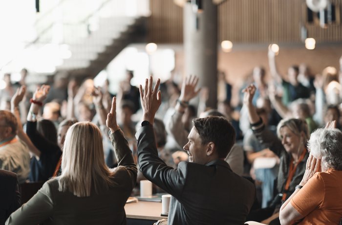 Eine große Versammlung, der Großteil der abgebildeten Menschen meldet sich