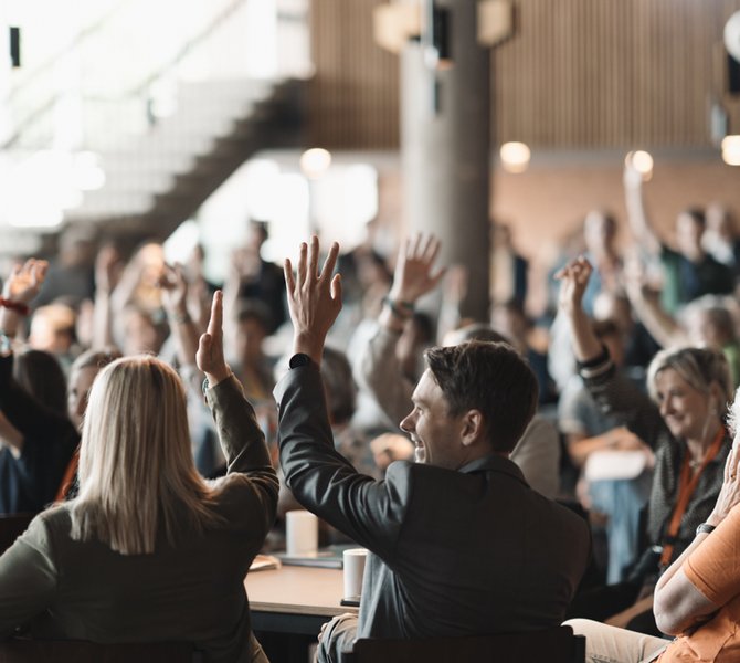 Eine große Versammlung, der Großteil der abgebildeten Menschen meldet sich