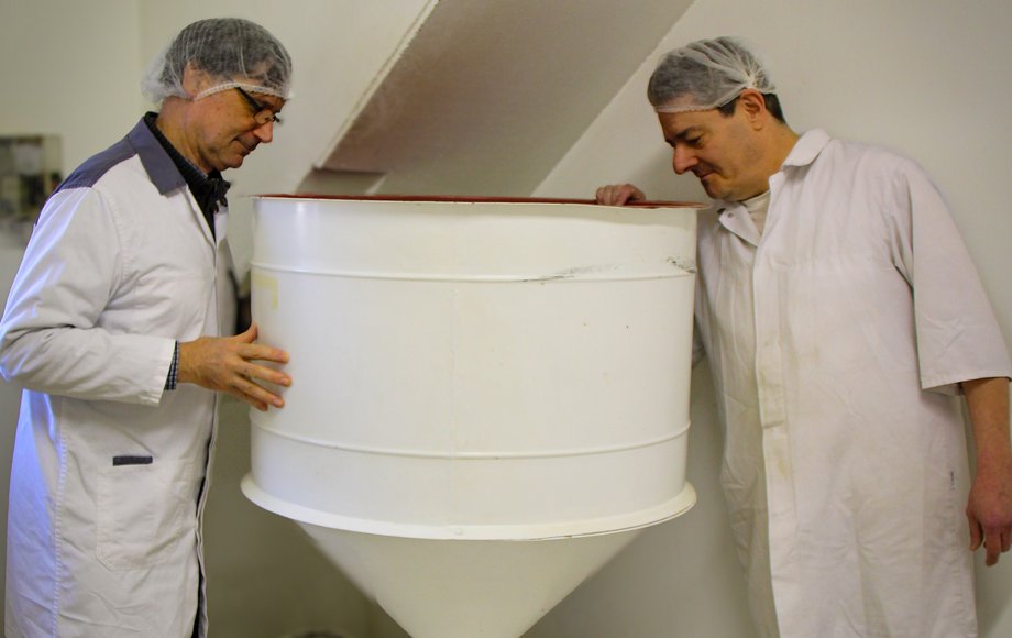 Blick in die Manufaktur der Feinkostfirma Steck: Zwei Mitarbeiter in weißen Kitteln und mit Haarnetzen begutachten eine große weiße Steinmühle.