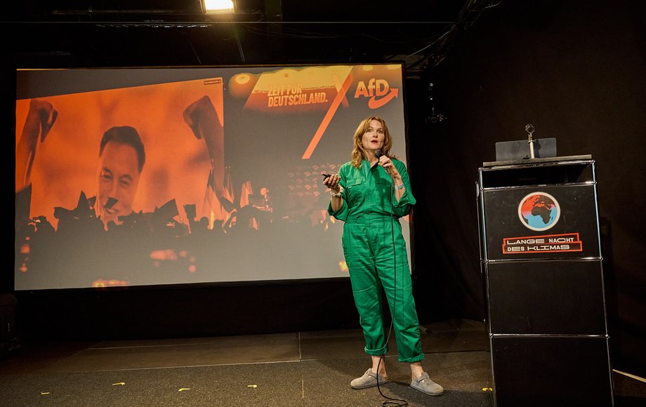 Frau im grünen Overall auf der Bühne vor Projektion