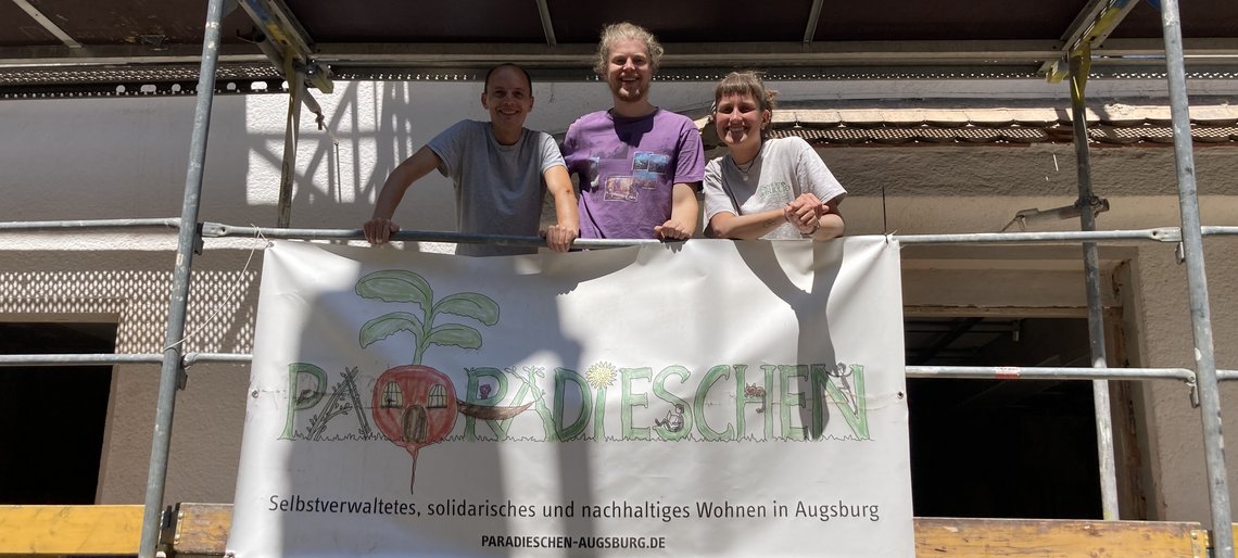Drei Menschen stehen auf einem Baugerüst