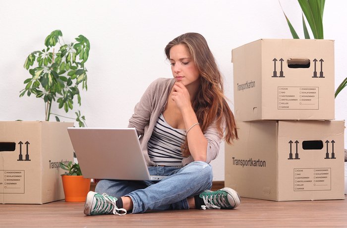 Frau mit Laptop sitzt zwischen Umzugskisten