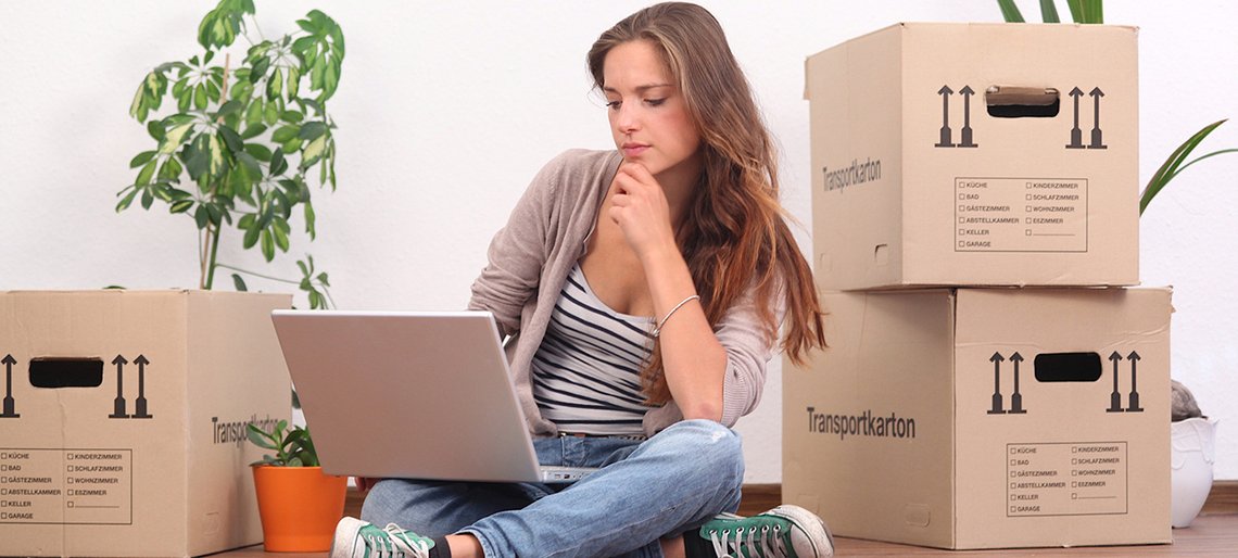 Frau mit Laptop sitzt zwischen Umzugskisten