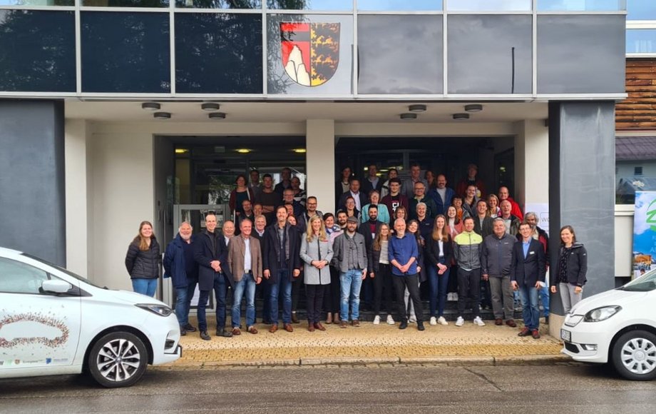 Gruppenfoto vor einem Rathaus, eingerahmt von zwei Autos