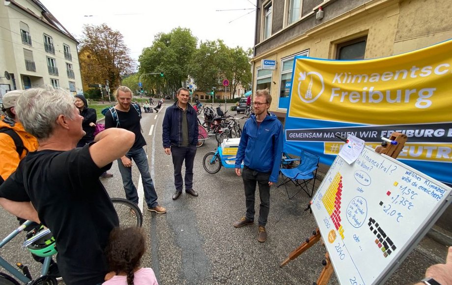 Mann steht an Stand auf der Straße, um ihn herum Menschen