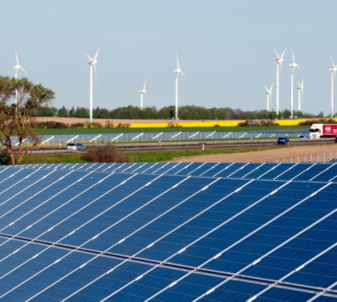 Windkrafträder und Solarmodule in einem Rapsfeld 