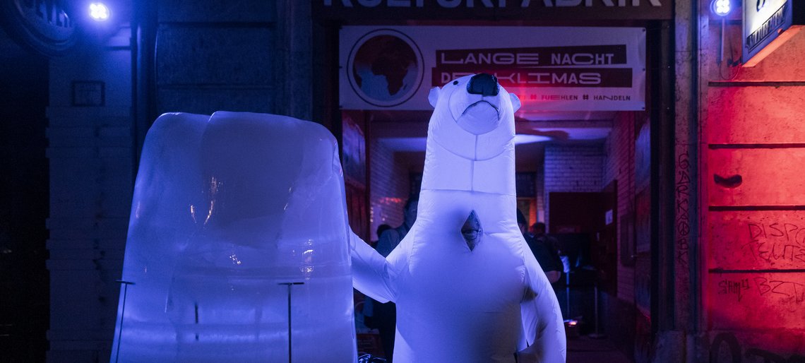 Eine Eisskulptur steht vor einem bunt erleuchteten Toreingang, daneben ein Mensch im Eisbärenkostüm