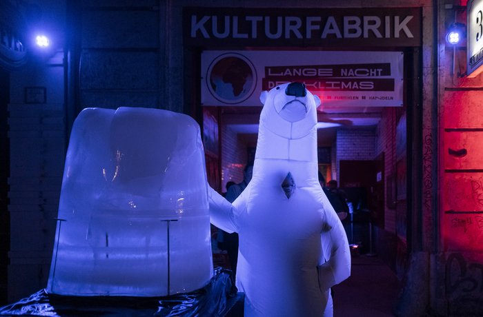 Eine Eisskulptur steht vor einem bunt erleuchteten Toreingang, daneben ein Mensch im Eisbärenkostüm
