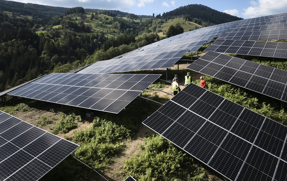 Solaranlage im Solarpark Fröhnd auf einem Berghang mit vier Menschen in Warnwesten, bewaldete Berglandschaft im Hintergrund.