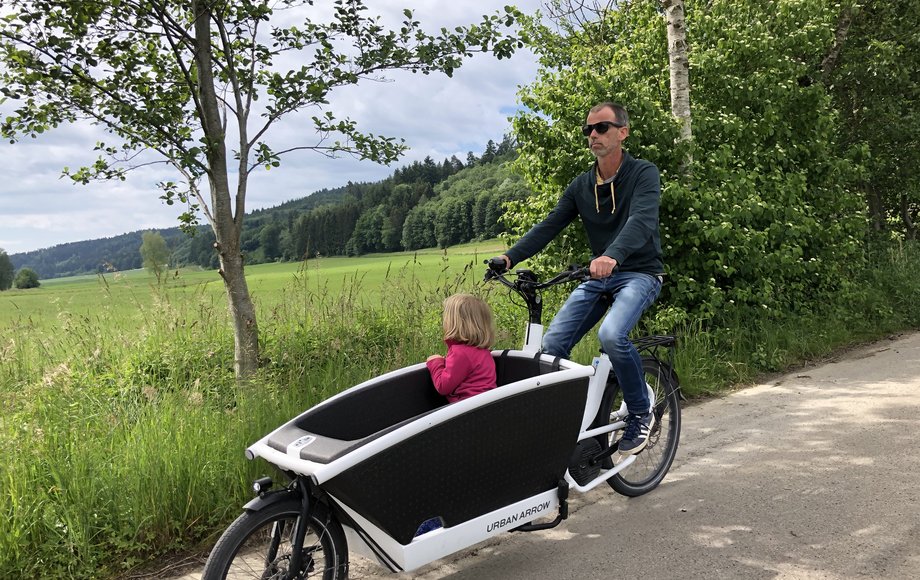 Mann im elektrischen Lastenrad mit einem mitfahrenden Kind 