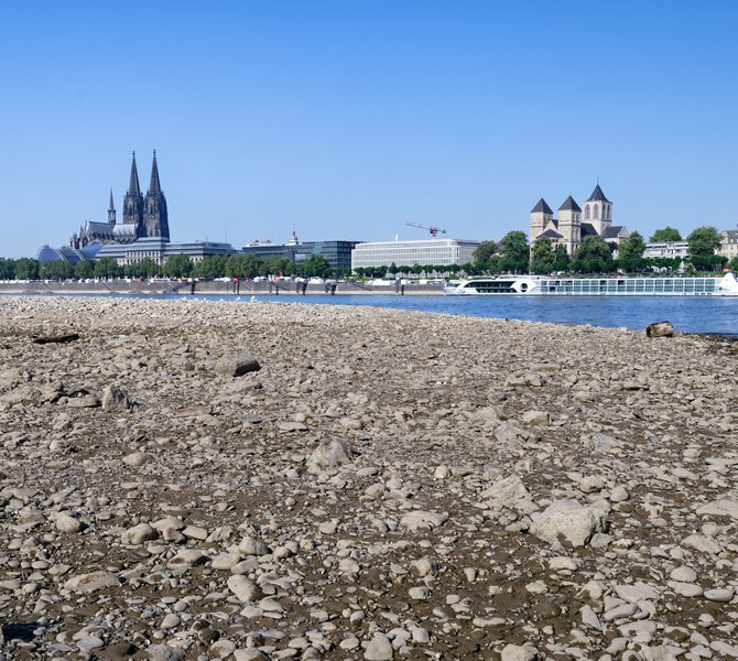 Panorama des Kölner Rheinufers bei Niedrigwasser, mit Dom, Hohenzollernbrücke und Ausflugsschiffen.