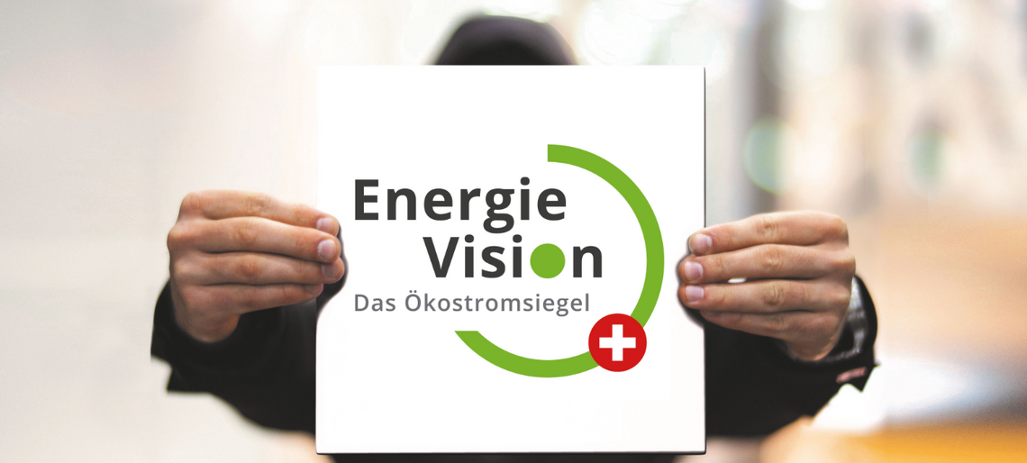 Eine Person hält ein Schild mit dem Logo des Ökostromsiegels EnergieVision-plus vor das Gesicht.