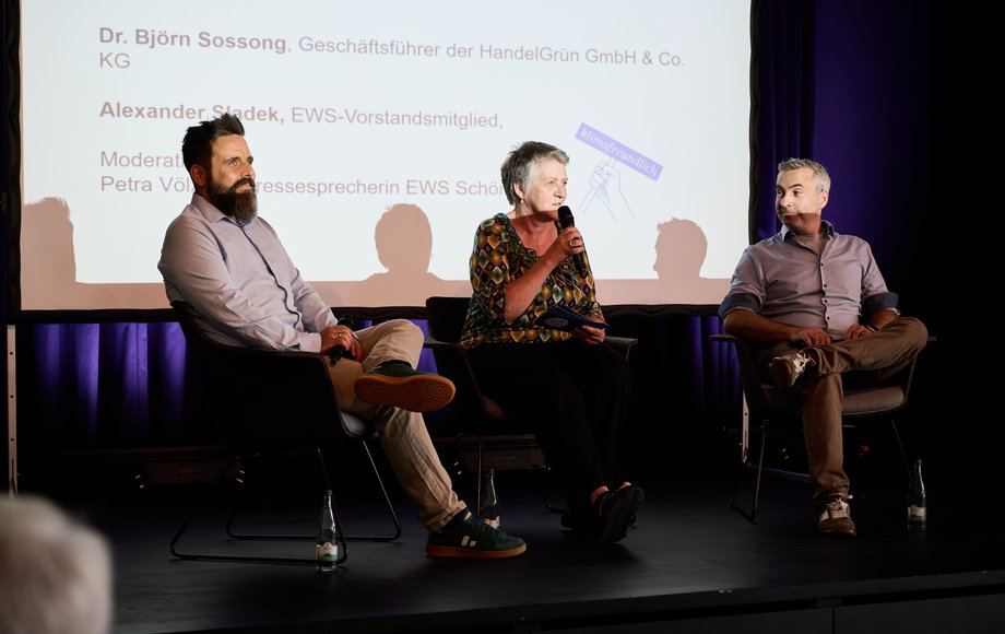 Drei Menschen sitzen im Halbkreis auf einer Bühne.
