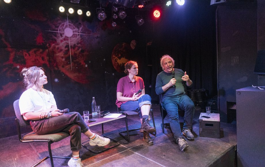 Zwei Frauen und ein Mann sitzen nebeneinander auf der Bühne auf Stühlen.