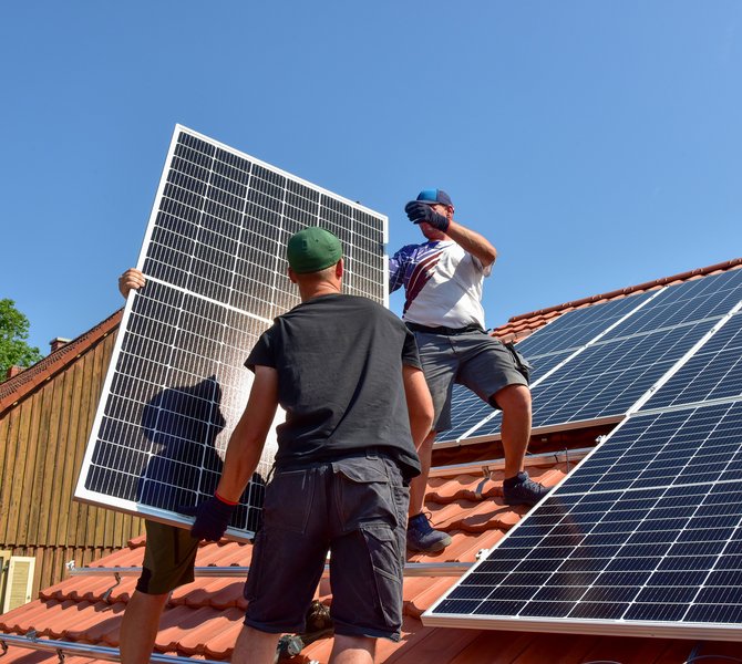 Drei Männer stehen auf einem Dach und tragen ein Solarpaneel