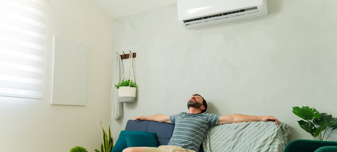 Mann hängt auf dem Sofa und genießt die Luft aus der Klimaanlage